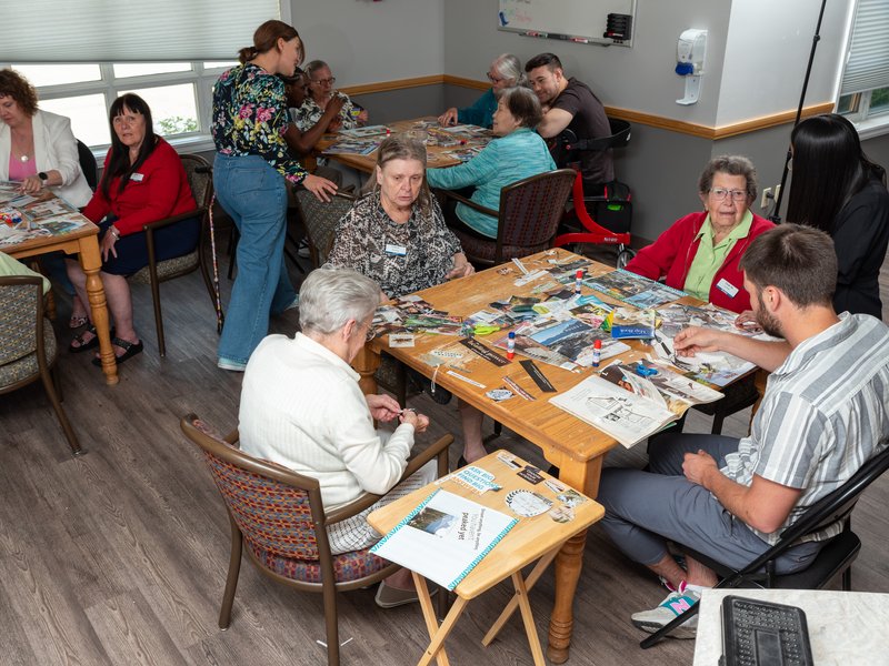 A group of seniors and helpers sitting at tables and making collages