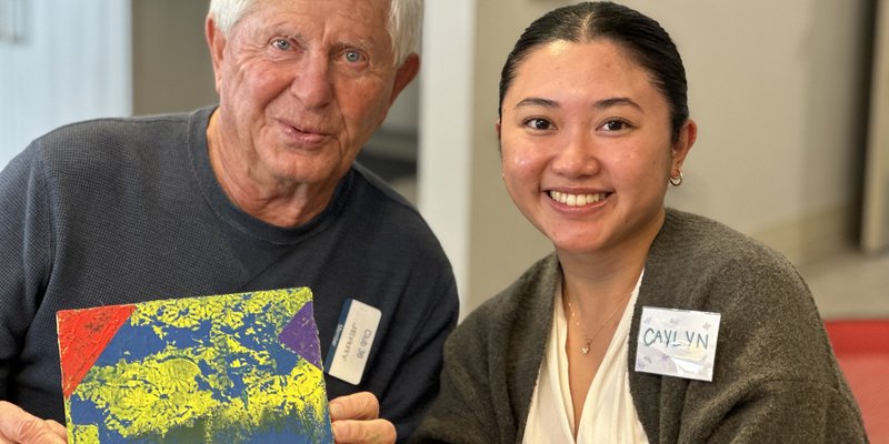 a senior smiling and holding a painter next to a smiling care partner